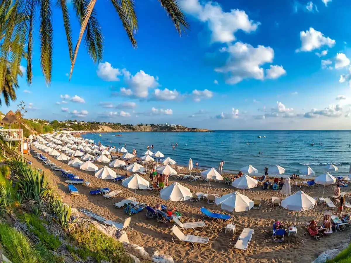 Słoneczne pafos plaże z białymi parasolami i leżakami, turkusowe morze i błękitne niebo z chmurami.