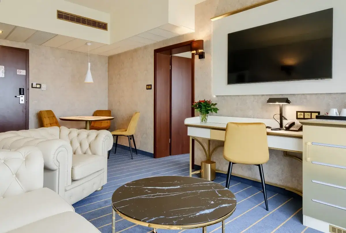 Elegancki pokój w hotelu Diament Wrocław: wygodna sofa, stolik kawowy, biurko z telefonem i TV, a także kącik jadalniany.