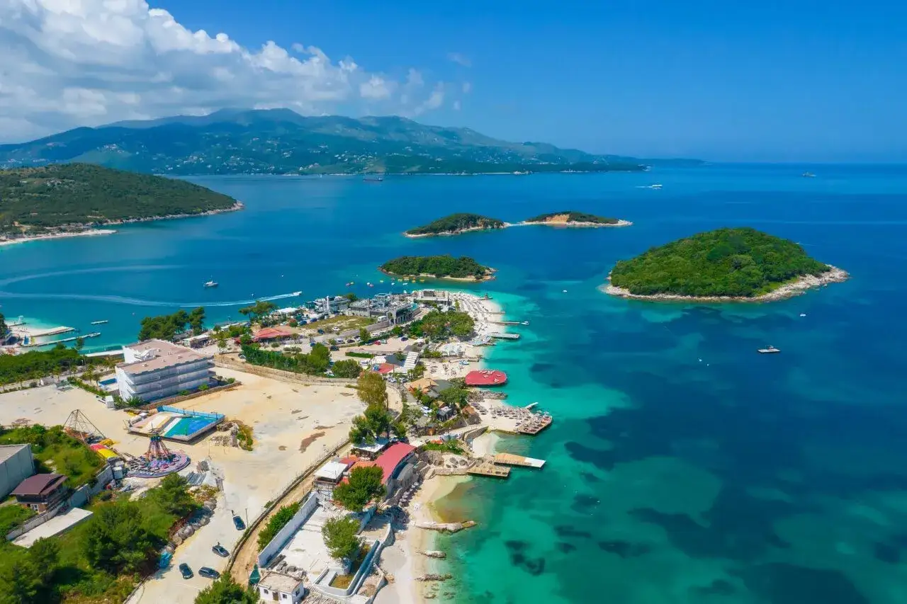 Rajska plaża z wysepkami, idealne miejsce na albania wakacje. Turkusowa woda, hotele i zielone wzgórza tworzą malowniczy krajobraz.