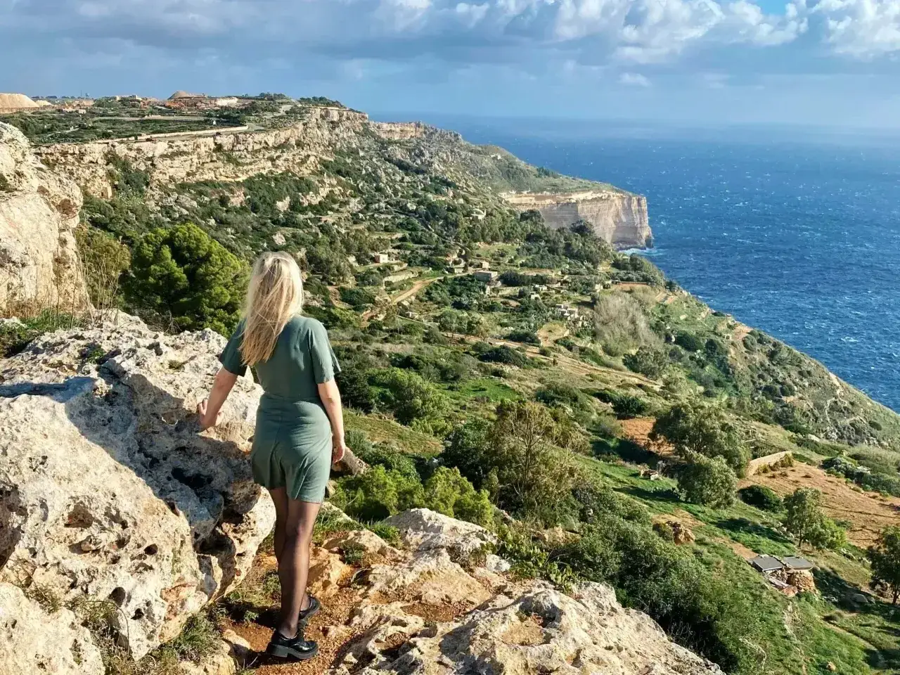 Malta pogoda w lutym: kobieta podziwia klify i morze. Zielone wzgórza i błękitna woda tworzą malowniczy krajobraz.