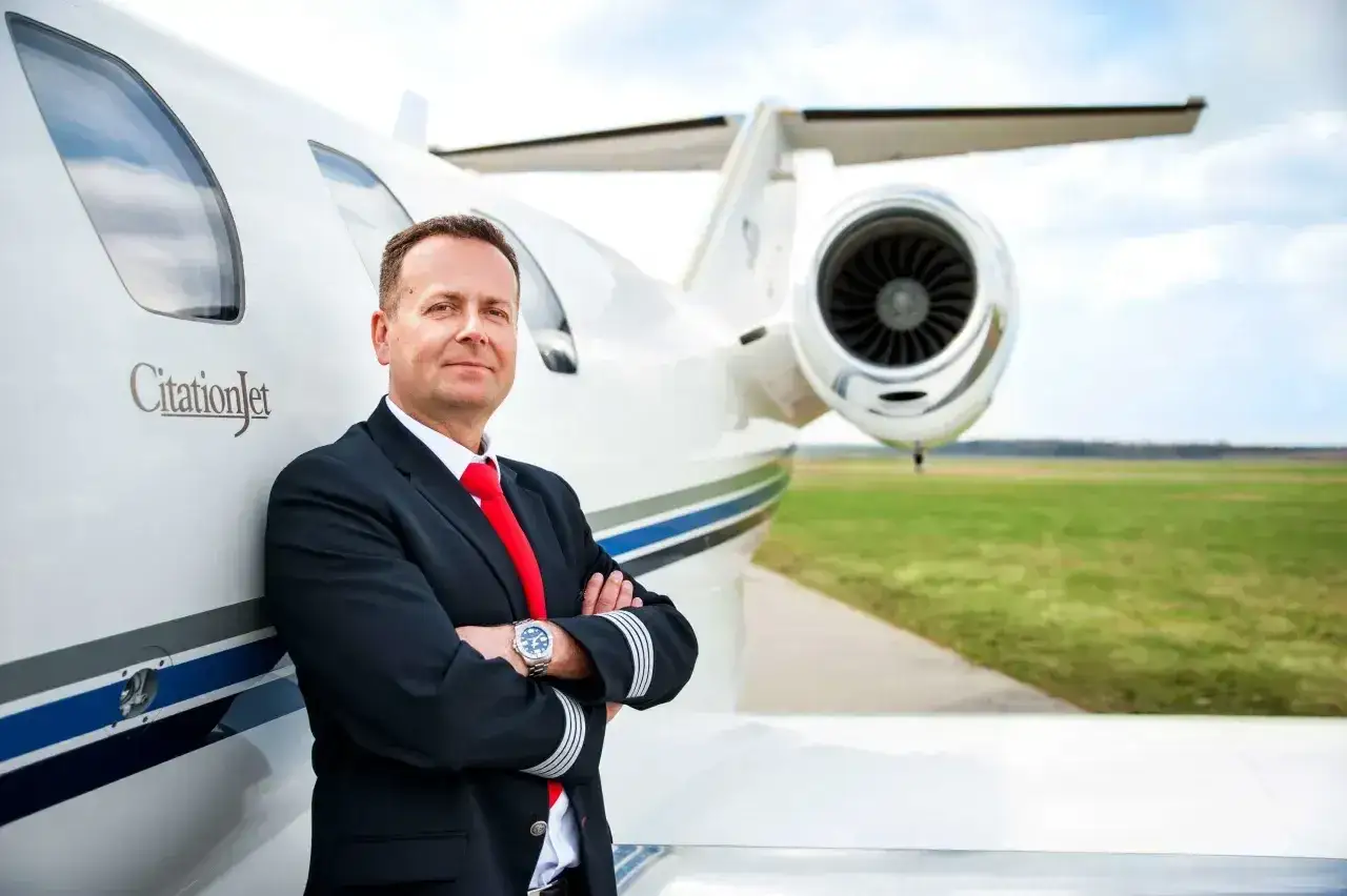 Pilot w mundurze z odznaką na rękawie, oparty o samolot CitationJet. Marzysz, jak zostać pilotem? To zdjęcie inspiruje!