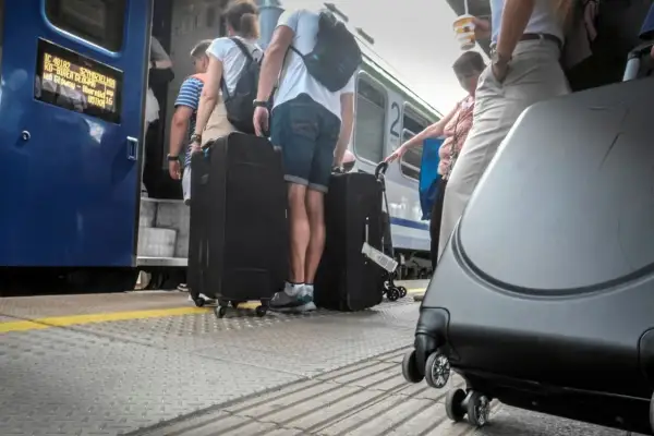 Ludzie z dużymi walizkami na peronie PKP, wsiadający do pociągu.