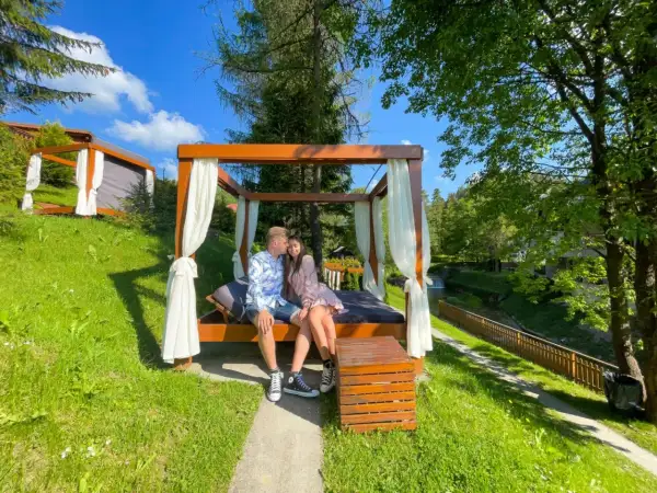 Idealne miejsce, gdzie na weekend we dwoje. Para odpoczywa na baldachimie z widokiem na strumyk i zieleń.