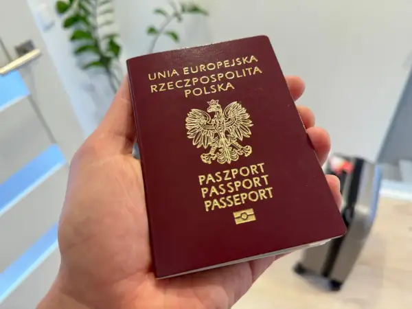 Dłoń trzyma polski paszport z godłem orła.