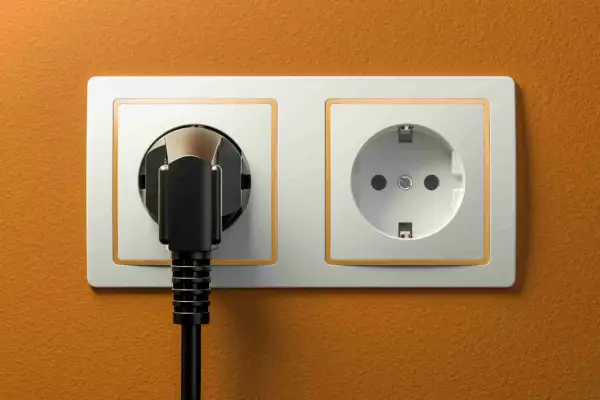 Dwa gniazdka elektryczne, jedno z wtyczką, na pomarańczowej ścianie. Typowe gniazdka w Hiszpanii.