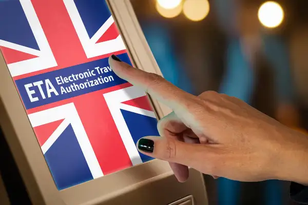Dłoń dotyka ekranu z flagą Wielkiej Brytanii, gdzie widnieje napis "ETA Electronic Travel Authorization". To formularz na wjazd do Anglii.